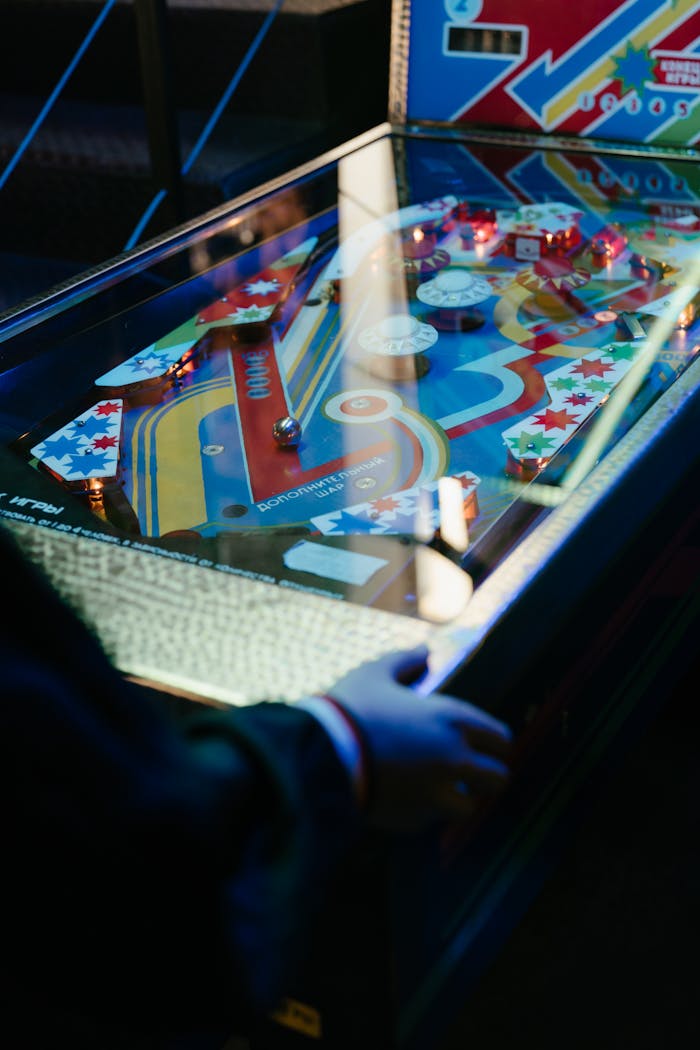 Colorful vintage pinball machine illuminated in a retro arcade setup with a player engaging.