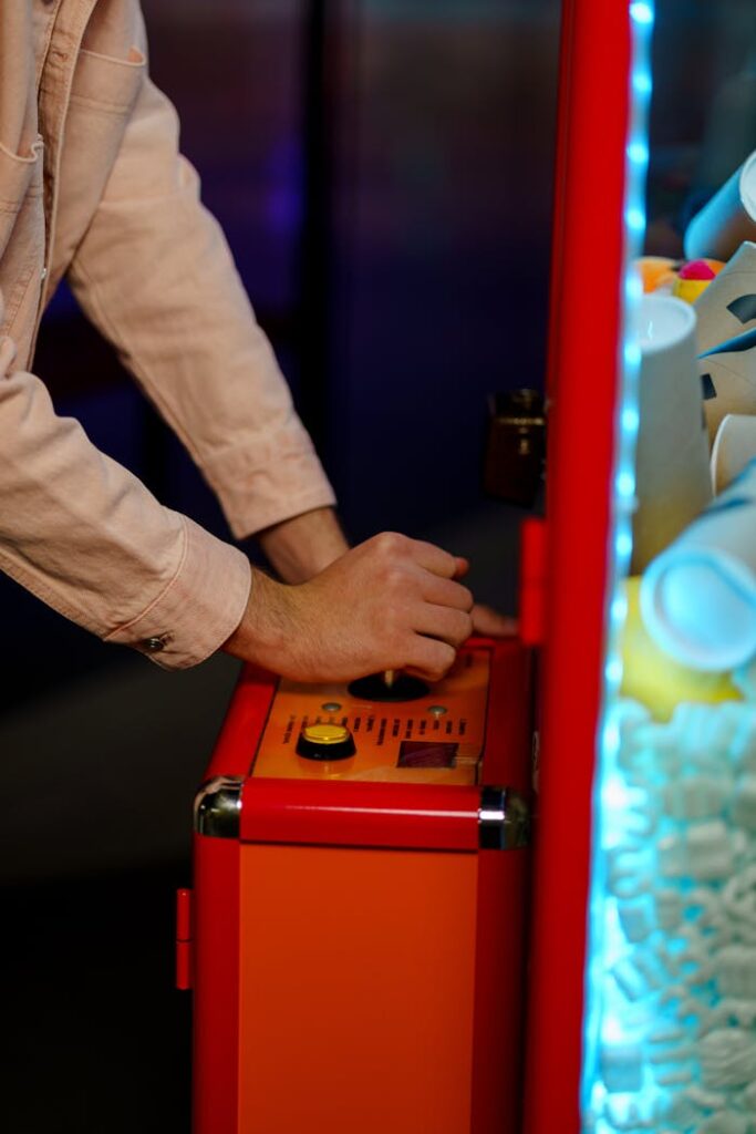 Close-up of a person operating a claw machine inside an arcade.